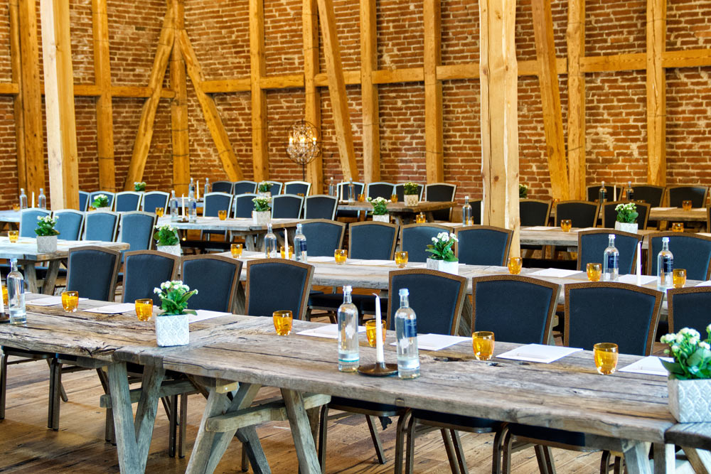 Seminarraum mit Holztischen und Stühlen, Wasserflaschen, Gläsern, Notizblättern und Blumendeko