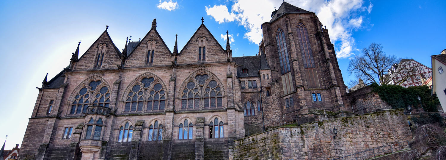 Historisches gotisches Gebäude mit großen Fenstern und Türmen vor blauem Himmel und ein paar Wolken