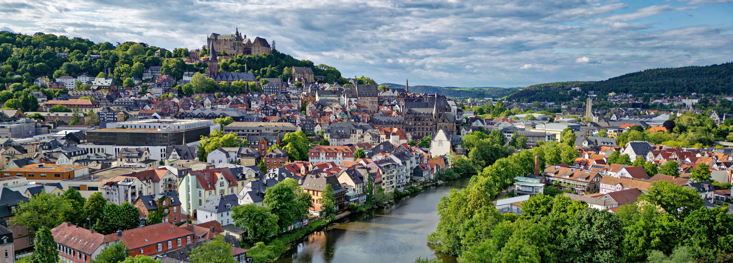 Stadtpanorama von Marburg mit der Lahn im Vordergrund und dem historischen Schloss auf einem Hügel im Hintergrund