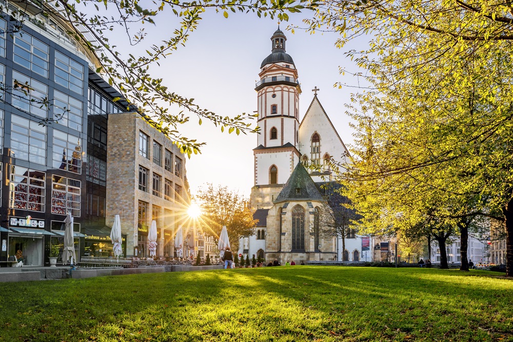 Historische Kirche mit Turm im Sonnenlicht neben modernen Gebäuden und grünem Park in einer Stadt
