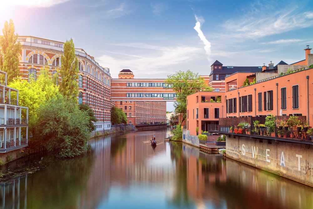 Industriearchitektur an einem Fluss mit begrünten Uferbereichen und Boot im Wasser bei Sonnenschein