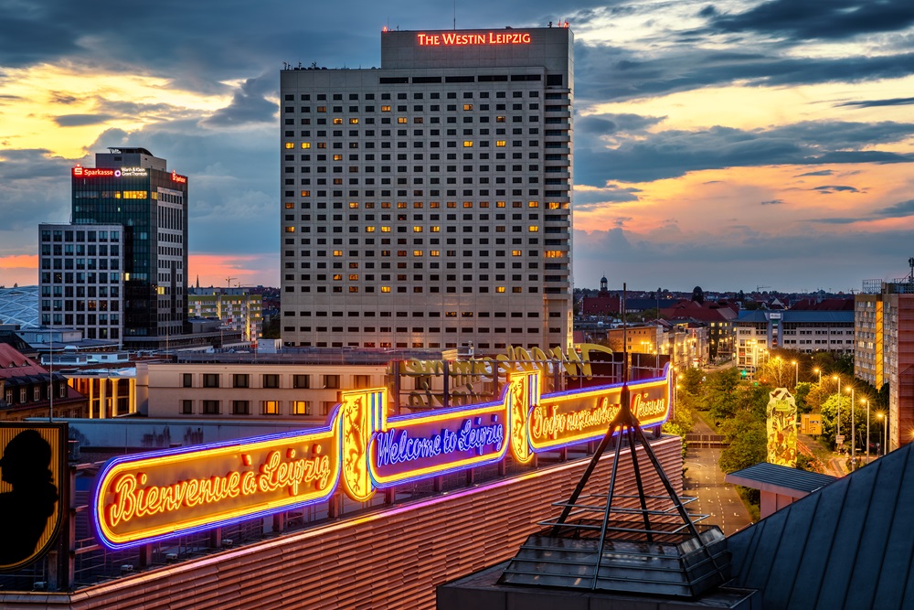 Stadtansicht von Leipzig bei Sonnenuntergang mit beleuchtetem Willkommensschild und Hochhäusern