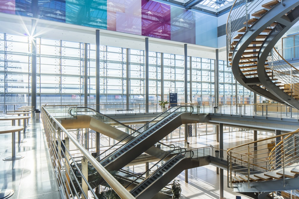 Modernes lichtdurchflutetes Atrium mit Glasfront, Treppen und farbigen Elementen unter der Decke