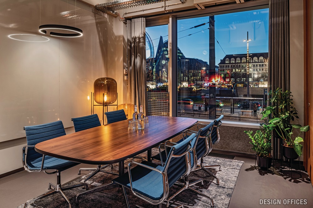 Moderner Meetingraum mit großem Holztisch, blauen Stühlen und Blick auf die beleuchtete Stadt