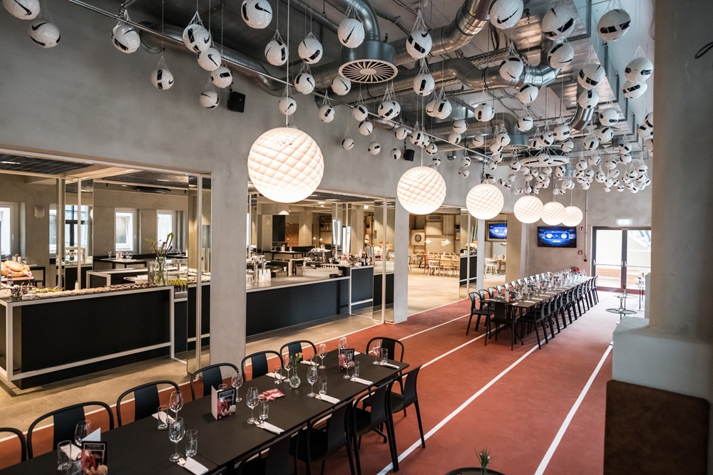 Modernes Restaurant mit langen Tafeln, Sportdeko und vielen Fußbällen an der Decke